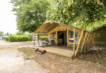 Safaritelt Harmony med overdækket træterrasse, havemøbler og grønne træer på campingplads.