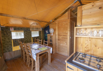 Intérieur d'une tente safari avec table à manger, chaises, gazinière et éléments en bois sous toile.