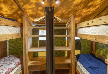 Interior de una tienda safari con literas y estanterías de madera en Camping Valkanela, Croacia.