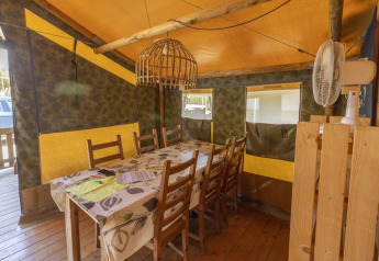 Zona pranzo nella Safaritent Sunset con sedie in legno e ventilatore al Camping Polari, Croazia.