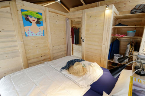 Schlafzimmer im Safarizelt mit Holzwänden, Doppelbett, Kleiderschrank und farbigem Wandbild.