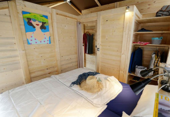 Camera in tenda safari con pareti in legno, letto matrimoniale, armadio aperto e quadro colorato.