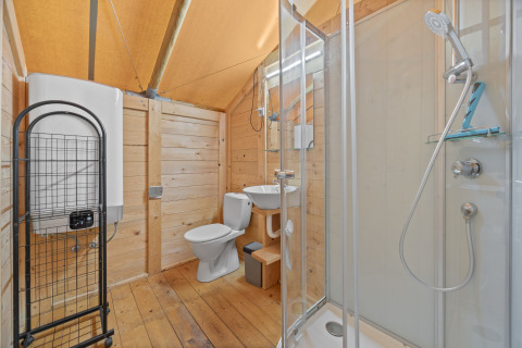 Salle de bain sous tente safari avec murs en bois, douche, toilettes et lavabo, offrant tout le confort.