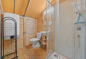 Bagno in tenda safari con pareti in legno, box doccia, WC e lavabo per un campeggio confortevole.