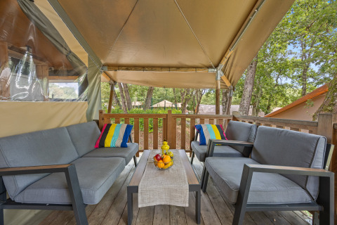 Buitenlounge in een safaritent met grijze zetels, kleurrijke kussens en fruitschaal op de houten tafel.