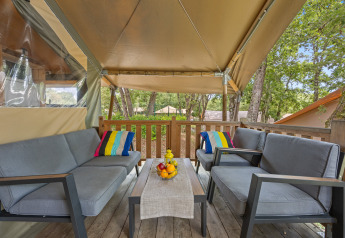 Gemütliche Sitzecke im Safarizelt mit grauen Sofas, bunten Kissen und Obstschale auf dem Tisch.