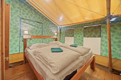 Binnenzicht van Safaritent Sunset op Camping Valkanela in Kroatië met tweepersoonsbed en houten vloer.