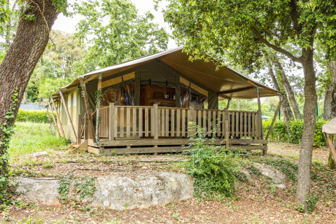 Tenda safari con veranda in legno immersa in una foresta verde, perfetta per il glamping.