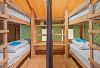 Interno di una tenda safari con letti a castello in legno, scaffali e asciugamani su ogni letto.