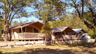 Tentes safari avec terrasses en bois sur muret de pierres, entourées d’arbres, ambiance nature et détente.