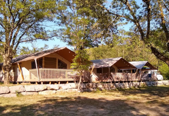 Tiendas safari con terrazas de madera sobre un muro de piedra, rodeadas de árboles para acampar cómodo.