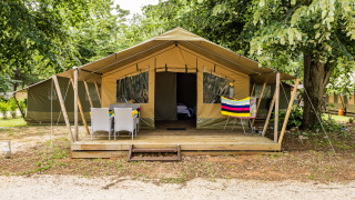 Safaritent Harmony met houten terras, tuinmeubels en kleurrige handdoek onder groene bomen.