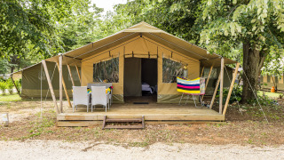 Tente safari Harmony avec terrasse en bois, mobilier de jardin et serviette colorée sous des arbres verts.