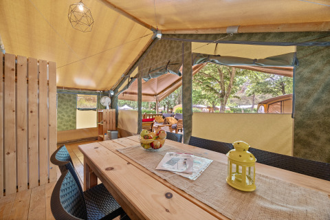 Vista interior de la Safaritent Relax con mesa de madera, sillas, decoración y ventanas abiertas al exterior.