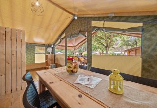 Vista interior de la Safaritent Relax con mesa de madera, sillas, decoración y ventanas abiertas al exterior.
