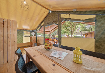Innenansicht des Safaritent Relax mit Holztisch, Stühlen, Dekoration und Ausblick auf Bäume draußen.