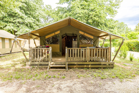 Tente safari avec véranda couverte en bois et garde-corps, entourée de verdure, vue de face.