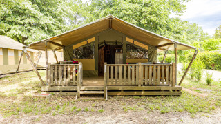 Tenda safari con veranda coperta in legno e ringhiera, immersa nel verde, vista frontale diurna.