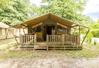 Tenda safari con veranda coperta in legno e ringhiera, immersa nel verde, vista frontale diurna.