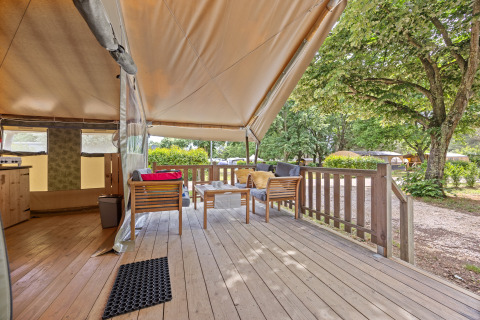 Vue sur une terrasse confortable avec meubles en bois et auvent de la Safaritent Relax sur un camping.