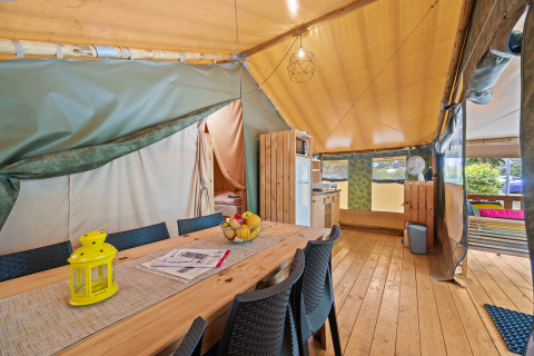 Binnenzicht van Safaritent Relax met houten tafel, stoelen, keukenhoek en warme tentinrichting.