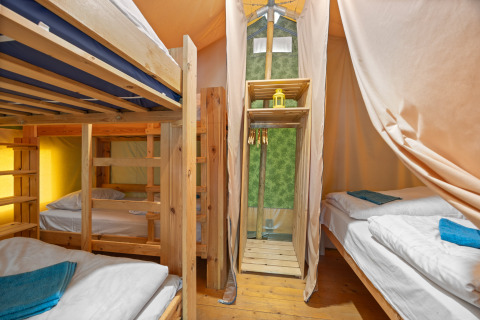 Interieur van Safaritent Relax met stapelbedden, enkele bedden, houten meubels en lichte gordijnen.