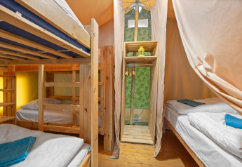 Innenraum des Safaritent Relax mit Etagenbetten, Einzelbetten, Holzmöbeln und hellen Vorhängen.