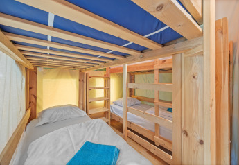 Vista interior de Safaritent Relax con literas de madera, sábanas blancas y toallas azules en la cama.