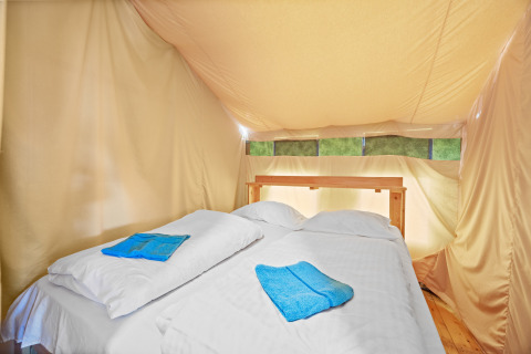 Slaapruimte in Safaritent Relax met dubbel bed, witte lakens en blauwe handdoeken in een canvas tent.