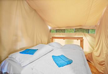 Zona notte nella Safaritent Relax con letto matrimoniale, lenzuola bianche e asciugamani blu in tenda.
