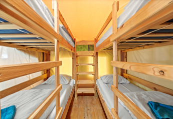 Vier eenpersoonsbedden in stapelbedopstelling in Safaritent Relax, met houten frames en licht interieur.