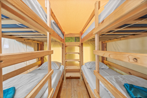 Quatre lits simples en disposition superposée dans la Safaritent Relax, avec cadres en bois et intérieur lumineux.