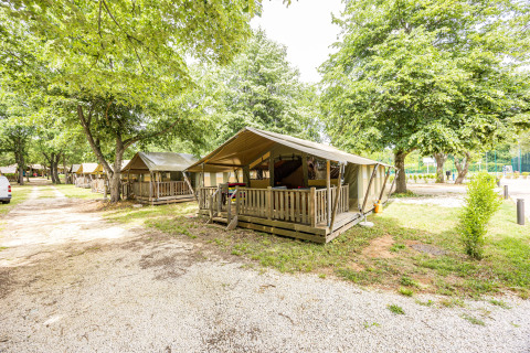 Safaritent Safaritent Relax met houten veranda, omgeven door bomen en andere soortgelijke tenten.