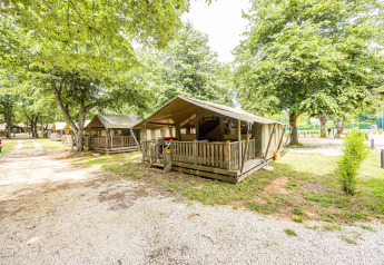 Tenda safari Safaritent Relax con veranda in legno, immersa tra alberi e altre tende simili.
