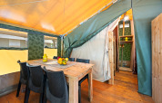 Interieur van Safaritent Relax met houten tafel, zwarte stoelen, fruitschaal en gele lantaarn op tafel.