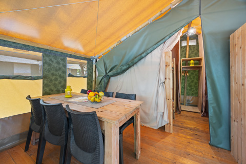 Vue intérieure de la Safaritent Relax avec table en bois, chaises noires, corbeille de fruits et lanterne jaune.
