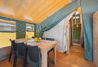 Vue intérieure de la Safaritent Relax avec table en bois, chaises noires, corbeille de fruits et lanterne jaune.