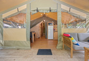 Interno della Safaritent Relax con cucina, divano con cuscini colorati e arredamento in legno.