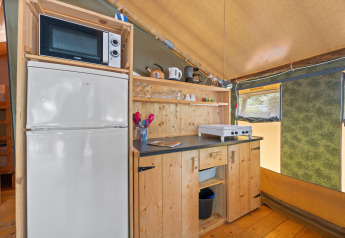 Angolo cucina nella Safaritent Relax con microonde, frigorifero, fornello e scaffali in legno dentro la tenda.