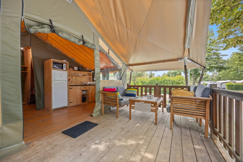 Vue du Safaritent Relax, tente safari avec terrasse en bois, coin salon, cuisine et décor naturel verdoyant.