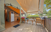 Tenda safari Safaritent Relax con terrazza in legno, area cucina e vista su alberi e natura circostante.