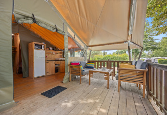 Tenda safari Safaritent Relax con terrazza in legno, area cucina e vista su alberi e natura circostante.