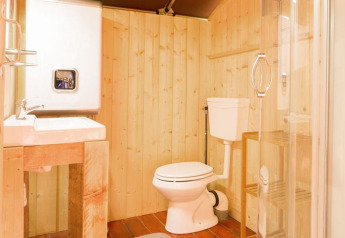 Bagno da tenda safari con pareti in legno, lavandino, WC e doccia con porta in vetro.