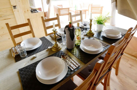 Tavola da pranzo elegante per sei in una tenda safari, con piatti, bicchieri e bottiglie di vino.
