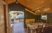 Intérieur d'une tente safari au Camping Lanterna, Croatie, avec table à manger, lampes et terrasse boisée.