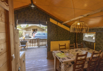 Interno di tenda safari al Camping Lanterna in Croazia con tavolo da pranzo, sedie e veranda esterna.