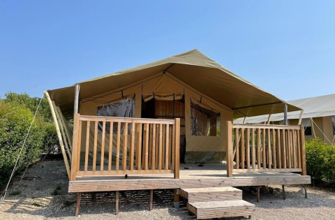 A safari tent with a spacious wooden deck and railings, set under a clear blue sky in a natural setting.