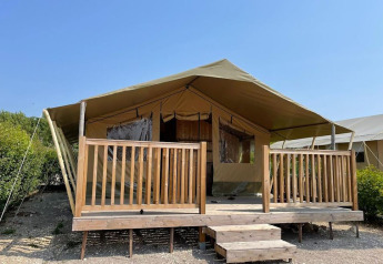 Tenda safari con ampia veranda in legno e corrimano, sotto un cielo azzurro in mezzo alla natura.