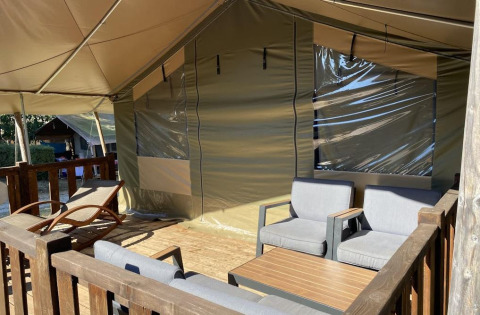 Zona relax all'aperto su terrazza di tenda safari con poltrone, tavolino e lettino prendisole in legno.