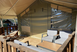 Gezellige zitruimte buiten aan een safaritent met comfortabele stoelen, tafel en ligstoel op het terras.